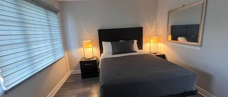 Quarto com uma cama grande, duas mesas de cabeceira com luminárias, um espelho na parede e uma janela com persianas.