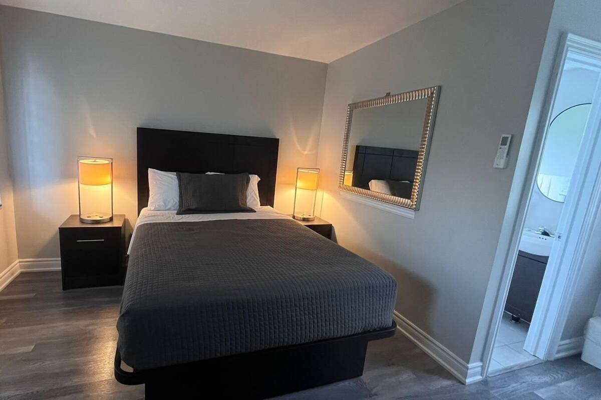 A bedroom with a large bed, two bedside tables with lamps, a mirror on the wall, and a door leading to a bathroom.