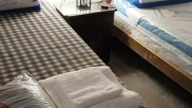 Una habitación con una colcha a cuadros, una cama con colchón azul y blanco, y una mesa con superficie negra.