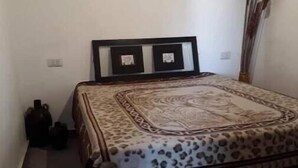 Un dormitorio con una cama, cuadros en la pared, un jarrón y una planta alta.