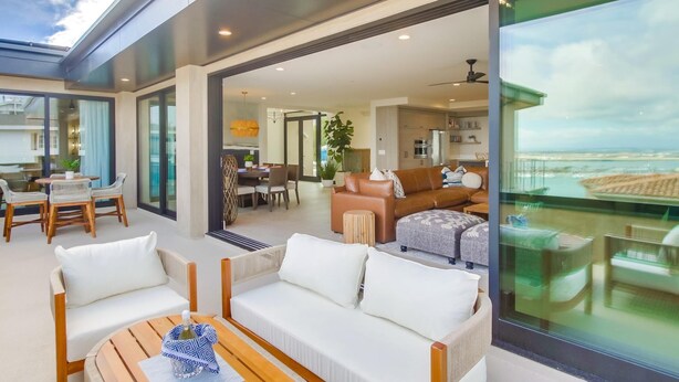 A modern living area with a sofa, chairs, and a dining table. There is a large window offering a view of the city. - Goldenview | 4BR Ocean, City & Bay Escape + Spa (San Diego)