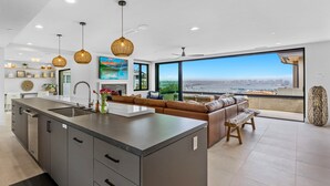 A modern kitchen with a large island, a dining area with a bench, and a large window offering a city view. - Goldenview | 4BR Ocean, City & Bay Escape + Spa (San Diego)