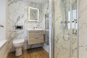A bathroom with a marble wall, a wooden vanity, a toilet, and a glass-enclosed shower area.