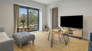 A modern living room with a large TV, a dining area with a table and chairs, and a sofa. - Quarry House, Aberporth (Aberporth)
