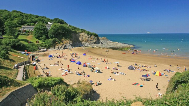 A beach with people sunbathing, tents, and a cliff with houses. - Quarry House, Aberporth (Aberporth)