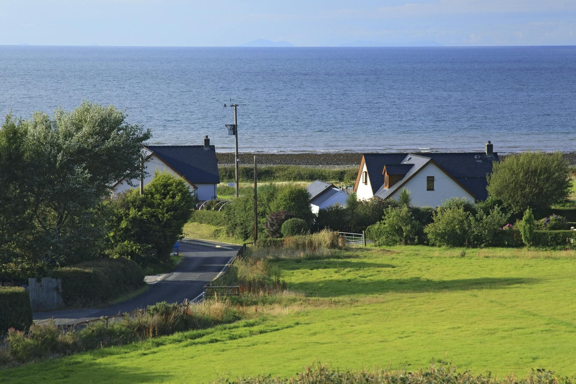 A coastal village with houses near the sea, a road, and lush greenery.