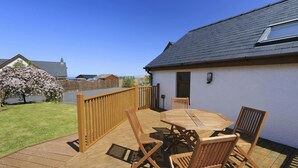 A wooden deck with a table and chairs, a wooden fence, and a house with a sloped roof. - Swn y Mor, Aberaeron (Aberaeron)