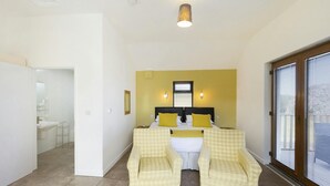 A bedroom with a bed, two bedside tables, a window with blinds, and a bathroom visible in the background. - Swn y Mor, Aberaeron (Aberaeron)