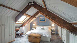 Une chambre à coucher avec un plafond en pente, un lit, des tables de chevet, un bureau, une chaise et une valise.