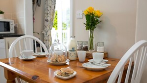 A wooden dining table with white chairs, a teapot, a milk bottle, a vase with yellow flowers, and various glass jars.