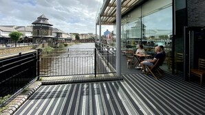 Un balcon donnant sur une rivière, un beffroi et un immeuble aux grandes fenêtres.