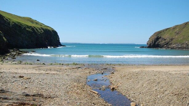Une plage rocheuse bordée par des vagues douces et entourée de falaises.