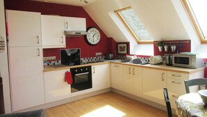 A compact kitchen with white cabinets, a black oven, a microwave, and a clock on the wall.