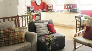 A cozy living room with a sofa, a dining table, and a kitchen in the background.