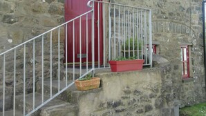 A stone building with a red door, a metal staircase with a railing, and a red flower pot on the steps.