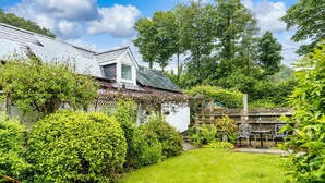 Un immobile residenziale con un giardino curato, una casa bianca con tetto a falde e un piccolo spazio esterno con sedie e tavoli in metallo.