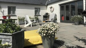 A patio with outdoor seating, potted plants, and a building with large windows and a garage door. - Ty Y Mor, Aberporth - Two Bedroom Cottage, Sleeps 4 (Aberporth)