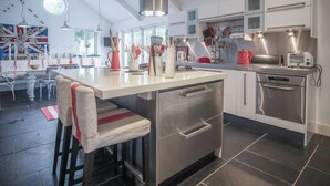 A modern kitchen with a central island, stainless steel appliances, and a dining area with a flag-themed wall. - Ty Y Mor, Aberporth - Two Bedroom Cottage, Sleeps 4 (Aberporth)