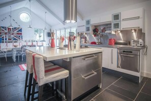 A modern kitchen with a central island, stainless steel appliances, and a dining area with a flag-themed wall. - Ty Y Mor, Aberporth - Two Bedroom Cottage, Sleeps 4 (Aberporth)