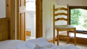 Una habitació amb un llit, una cadira de fusta i una finestra que dona a un espai verd.