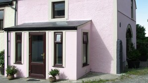 Una casa de color rosa amb un teulat fosc, una porta d'entrada i dues finestres.