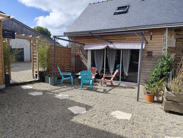 A wooden building with a gravel patio, two blue chairs, and a small table.