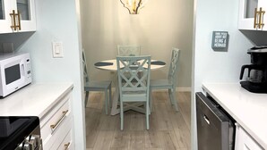 Een moderne keuken met witte kasten, een eettafel met stoelen, een magnetron, een koffiezetapparaat en een vaatwasser.