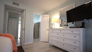 Een slaapkamer met een bed, een kaptafel, een televisie en een deur naar een andere kamer.