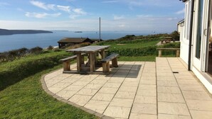 Une terrasse avec une table en bois et des bancs, d’où l’on peut admirer un plan d’eau et une île lointaine.