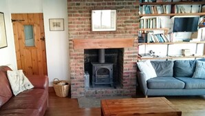 Un salon chaleureux avec une cheminée en briques, un canapé en cuir, un divan gris et une table basse en bois.