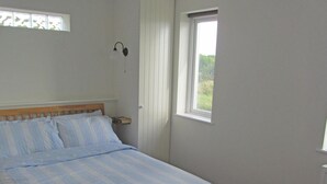Une chambre à coucher comprenant un lit, une table de chevet, une fenêtre et une lampe fixée au mur.