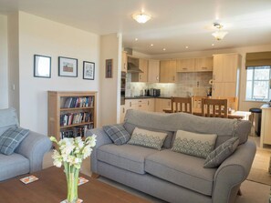 A living room with a grey sofa, a bookshelf, and a vase with flowers.