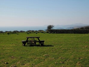 A picnic table in a grassy field with a view of the ocean and distant mountains.