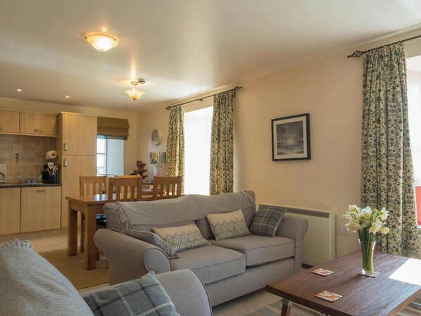 A cozy living room with a sofa, a dining table, and a kitchen in the background.