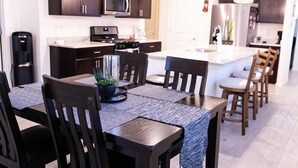 Une cuisine moderne avec des meubles de couleur sombre, un four à micro-ondes et une cuisinière. On y trouve un coin repas avec une table et des chaises, ainsi qu’un petit îlot central doté d’un évier.