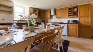 A modern kitchen with wooden cabinets, a dining table set for four, and a vase of white flowers. - The Stables, Newgale (Llandeloy)