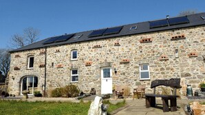 A stone building with multiple windows, a door, and a small outdoor seating area with benches. - The Stables, Newgale (Llandeloy)