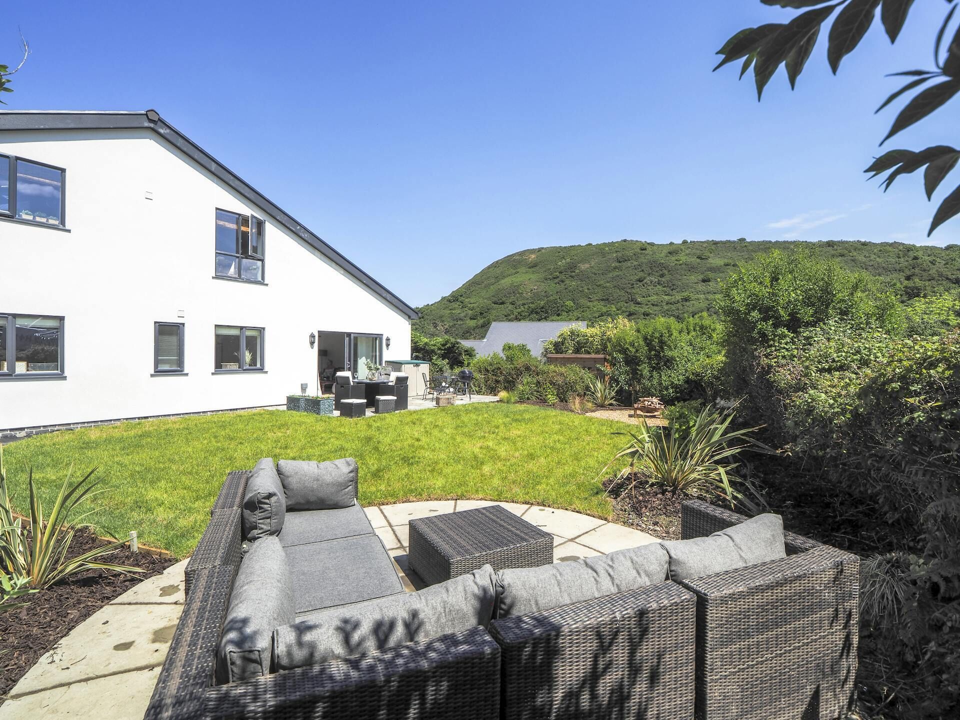 A modern house with a large patio area featuring a grey sofa set and outdoor furniture.