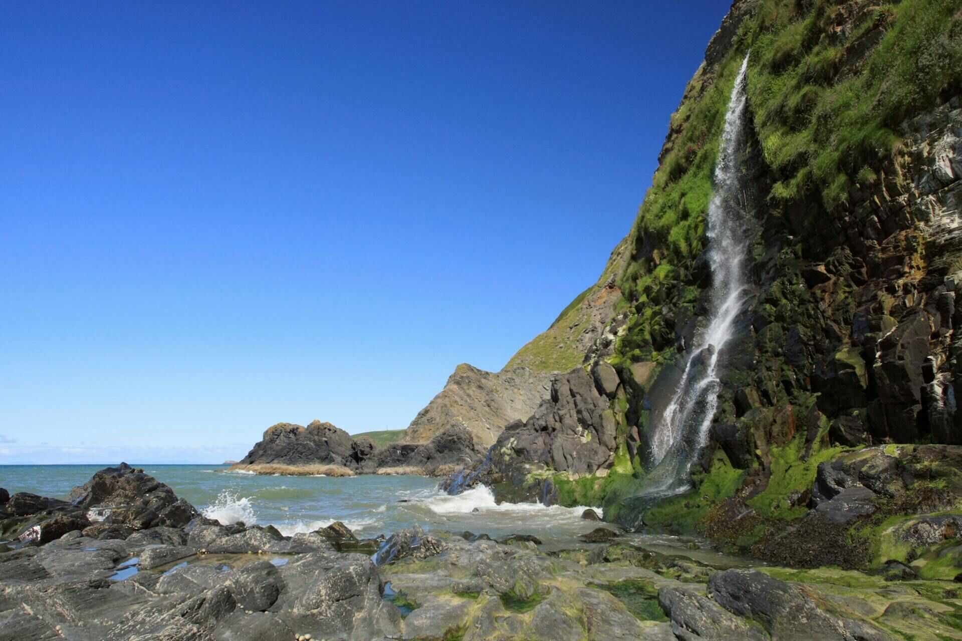 A coastal landscape with a waterfall, rocky shore, and ocean.