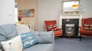 A living room with a grey sofa, two armchairs, a fireplace, and a painting on the wall. - No. 1 Cliffside, New Quay (New Quay)