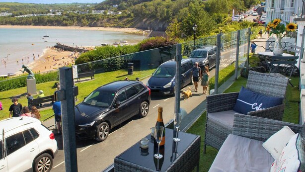 A coastal view with a beach, parked cars, and outdoor seating. - No. 1 Cliffside, New Quay (New Quay)