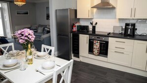 A modern kitchen with a refrigerator, oven, microwave, and a dining area with a table set for two. - No. 1 Cliffside, New Quay (New Quay)