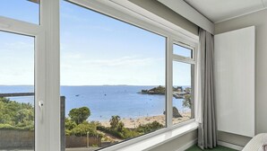 A room with a large window overlooking a beach and sea, a green carpet, and a white wall. - Puffins Nest, Tenby - Two Bedroom Cottage, Sleeps 4 (Tenby)