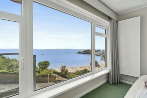 A room with a large window overlooking a beach and sea, a green carpet, and a white wall. - Puffins Nest, Tenby - Two Bedroom Cottage, Sleeps 4 (Tenby)