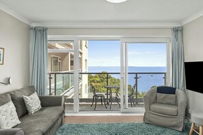 A living room with a sofa, armchair, and a view of the sea through a balcony.