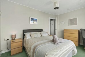 A bedroom with a bed, bedside tables, a lamp, a hanging light fixture, a door, and a chair. - Puffins Nest, Tenby - Two Bedroom Cottage, Sleeps 4 (Tenby)
