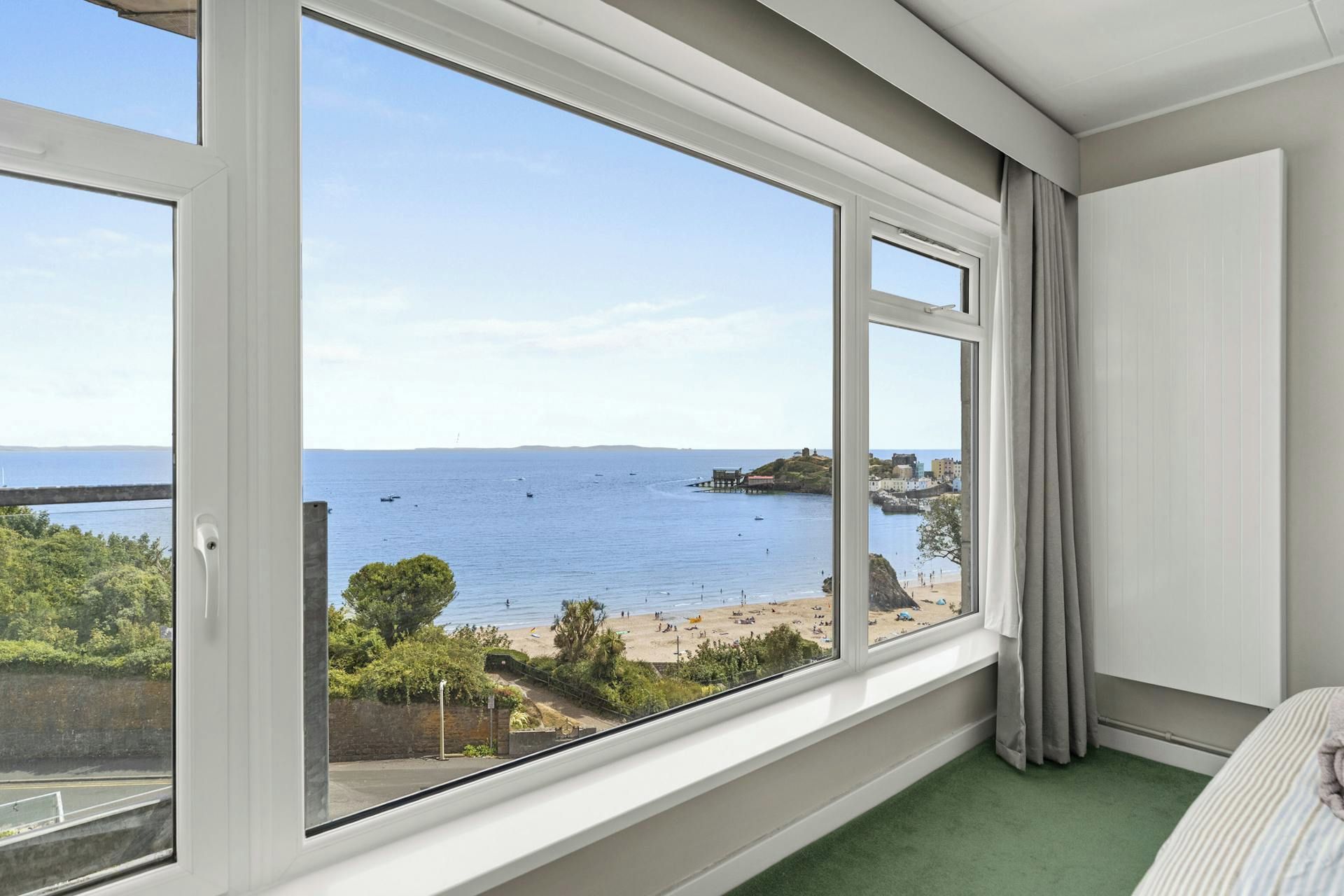 A room with a large window offering a view of a beach and the sea.