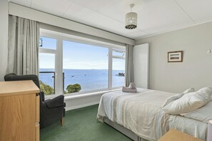 A bedroom with a bed, a chair, a desk, and a view of the sea.