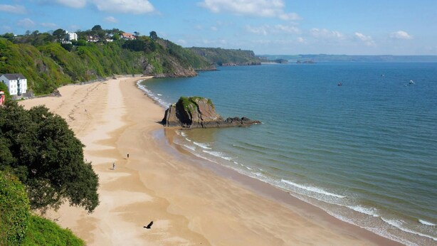 A coastal beach with a rocky outcrop, a clear sky, and houses on the hillside. - Puffins Nest, Tenby - Two Bedroom Cottage, Sleeps 4 (Tenby)