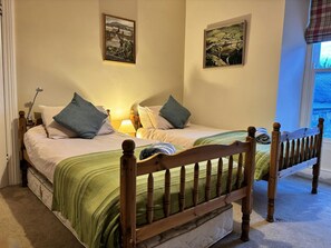 Un lit double avec une tête de lit en bois, deux oreillers, une couverture à rayures vertes et deux tableaux accrochés au mur.